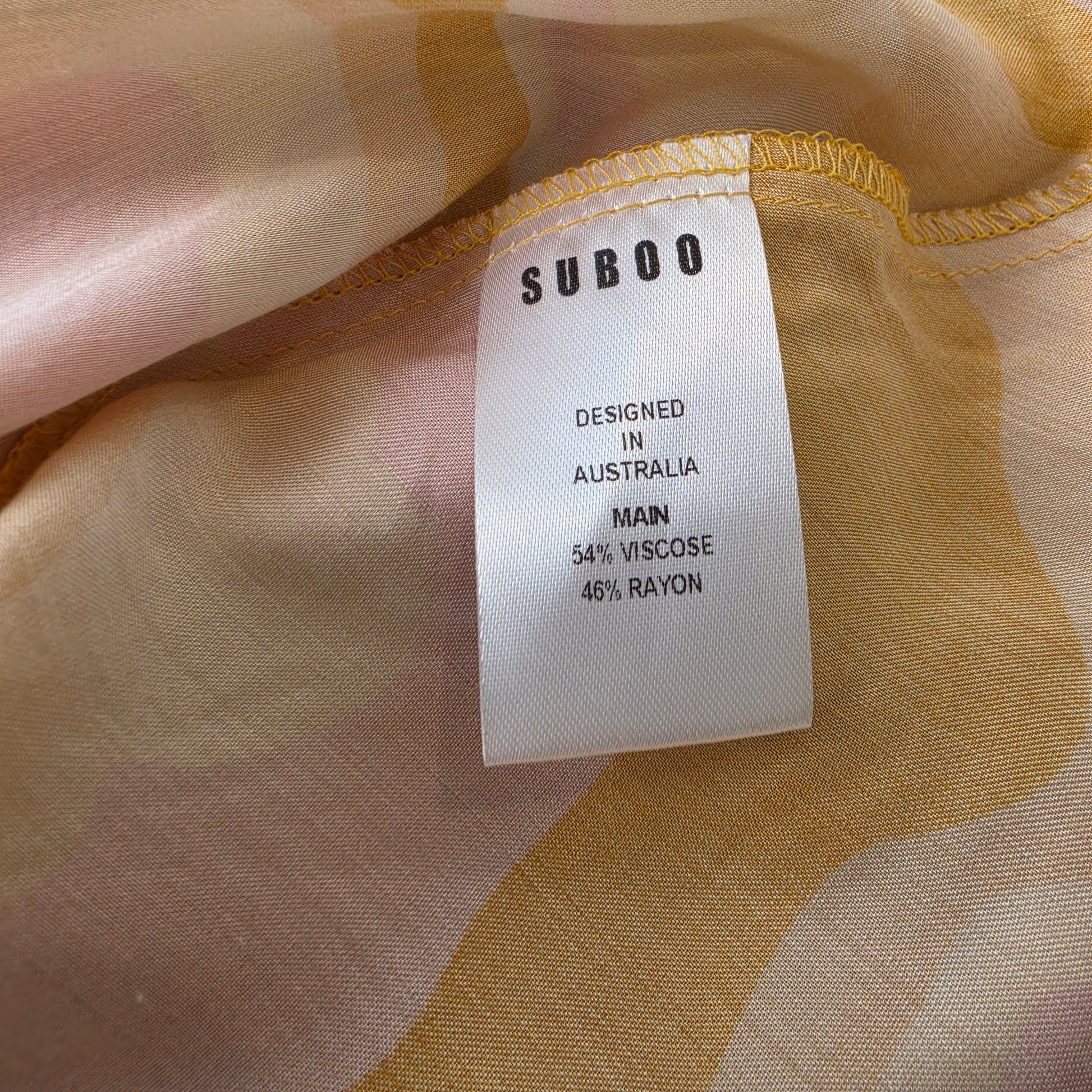 Close-up of a white fabric tag with black text reading 'SUBOO' and garment details, attached to the Suboo Cloud Keyhole Slip Dress