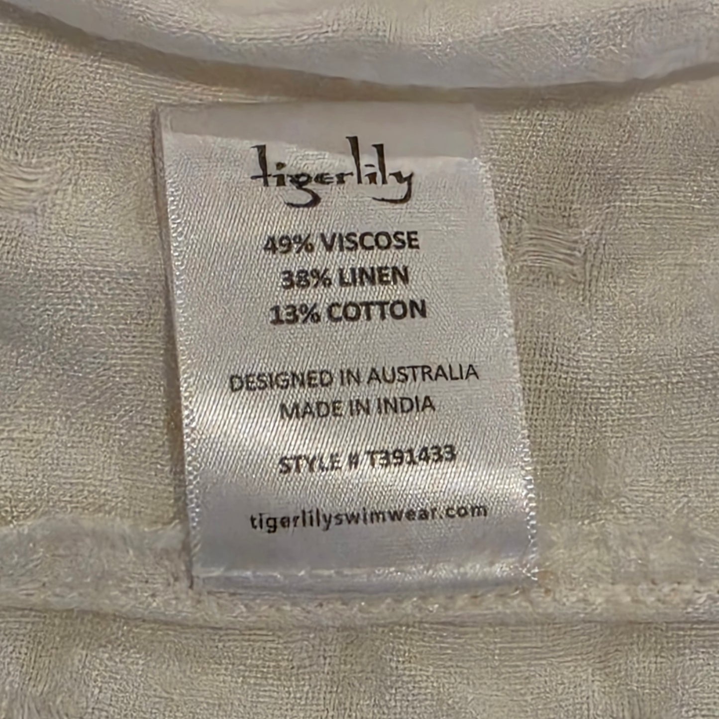 Close-up of a sewn-on fabric label reading Tigerlily with material percentages and product details, attached to the Tigerlily Avari Dress