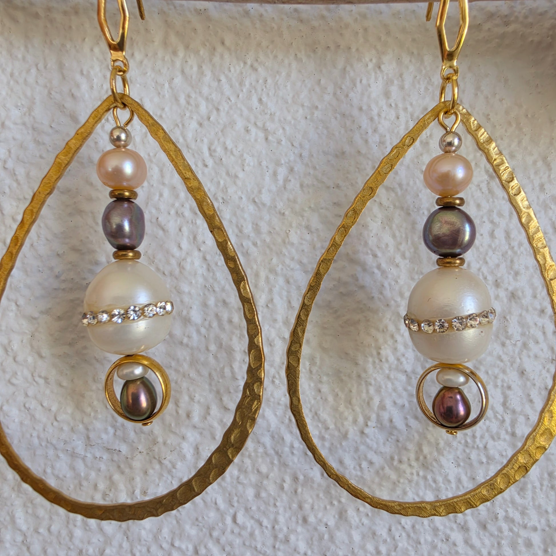 Close-up view of the versamel earrings showing the different coloured pearls, hammered brass and gold plated components.