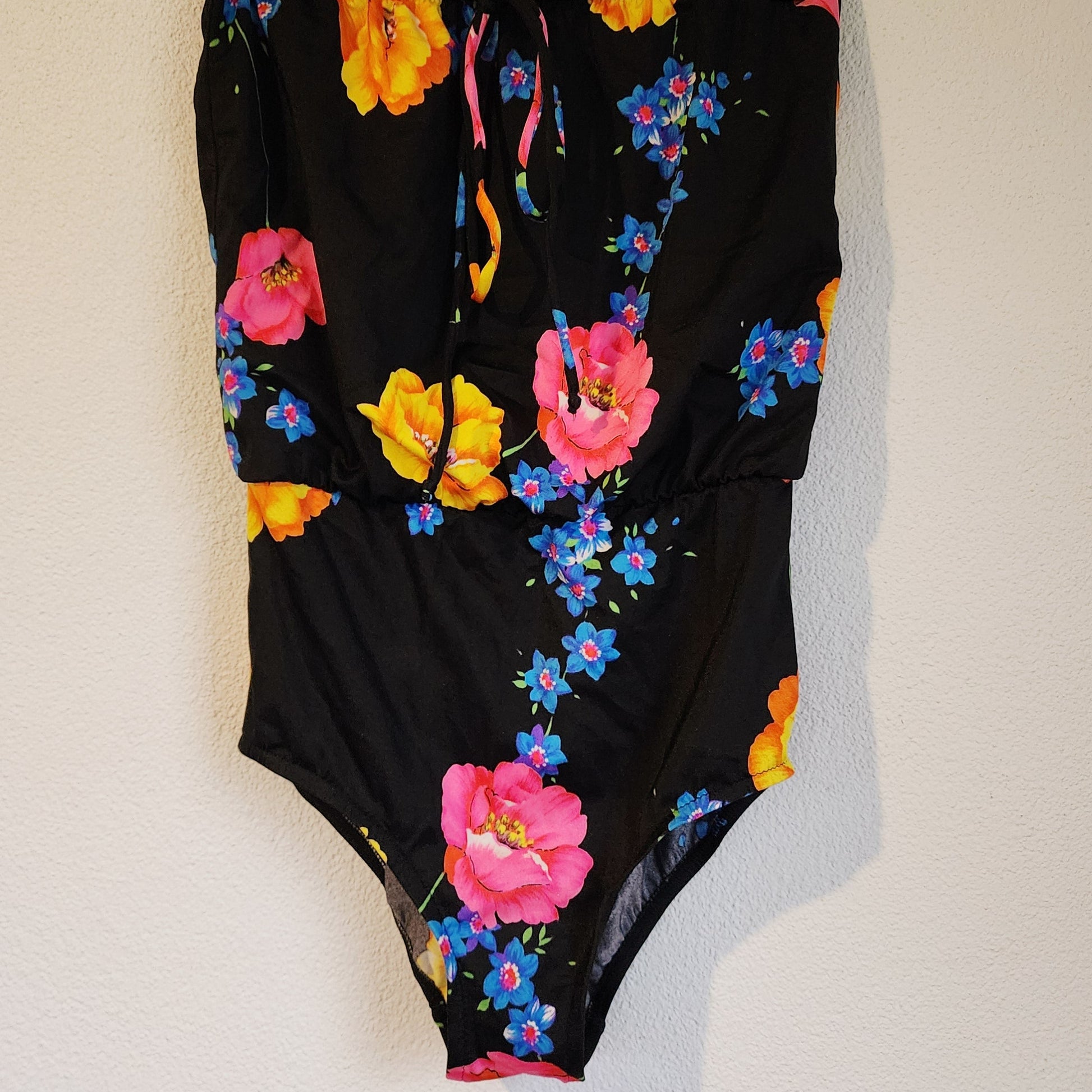 Front view of vintage black swimsuit with a colourful floral design on a white surface