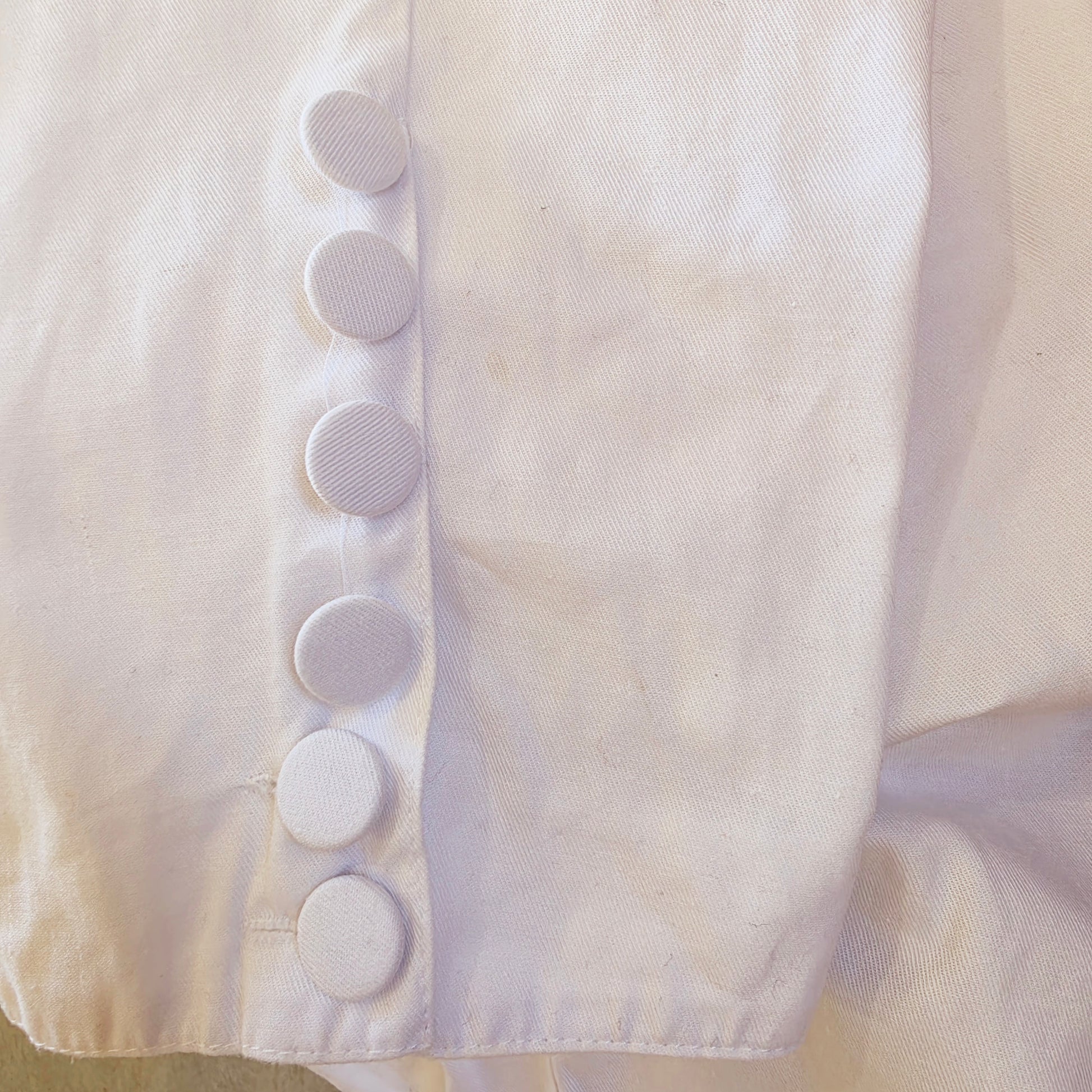 Close-up of fabric-covered button detail on the cropped cuff of vintage Katies white pants.