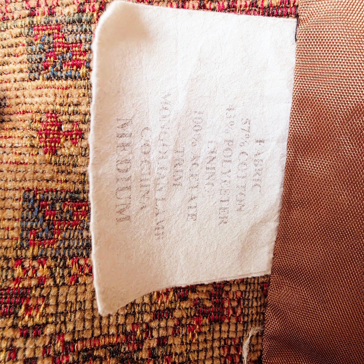 A close-up of a white fabric label sewn onto the vintage Penny Lane tapestry coat. 