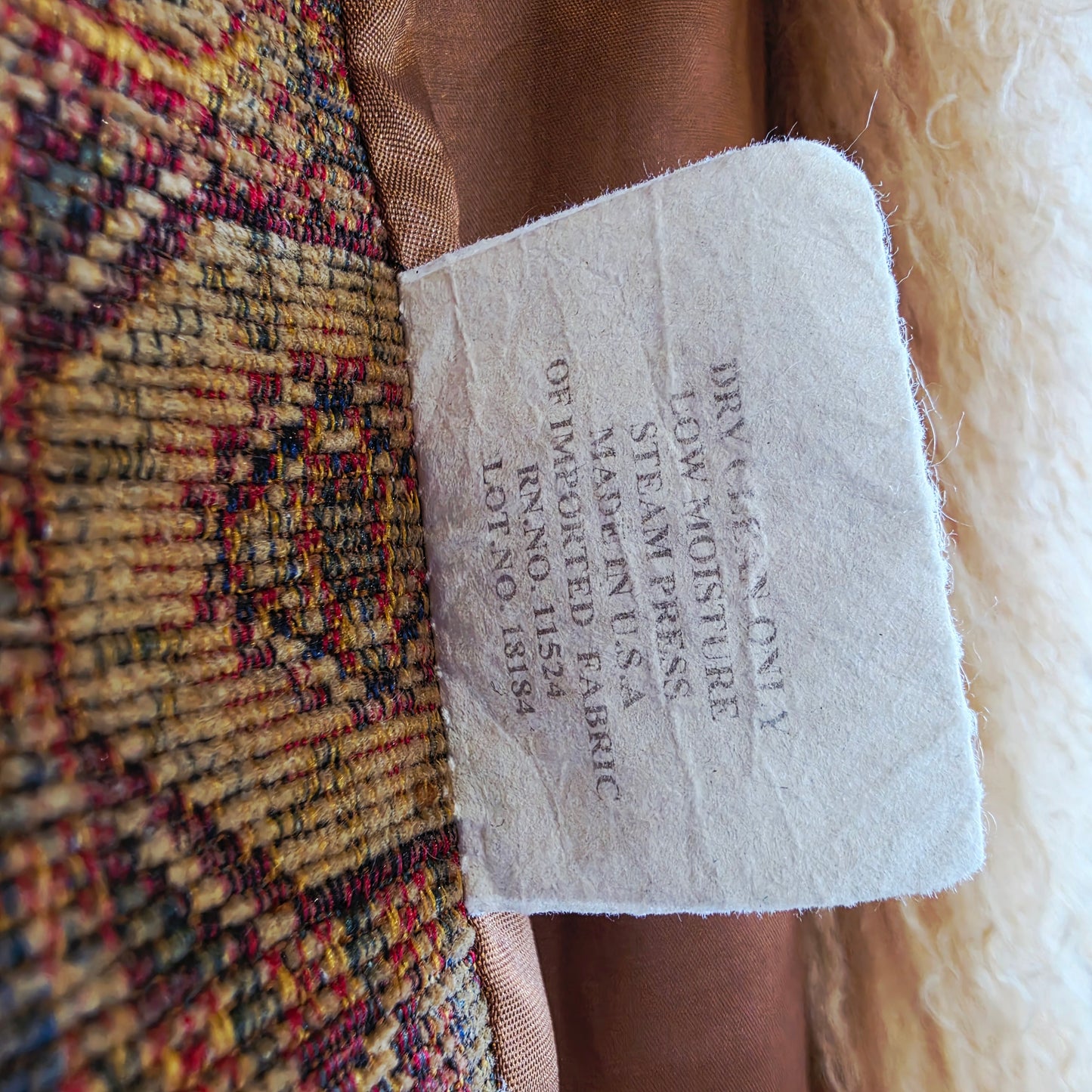 A close-up of a fabric label sewn onto the vintage Penny Lane tapestry coat, and printed text reading 'DRY CLEAN ONLY LOW MOISTURE STEAM PRESS MADE IN U.S.