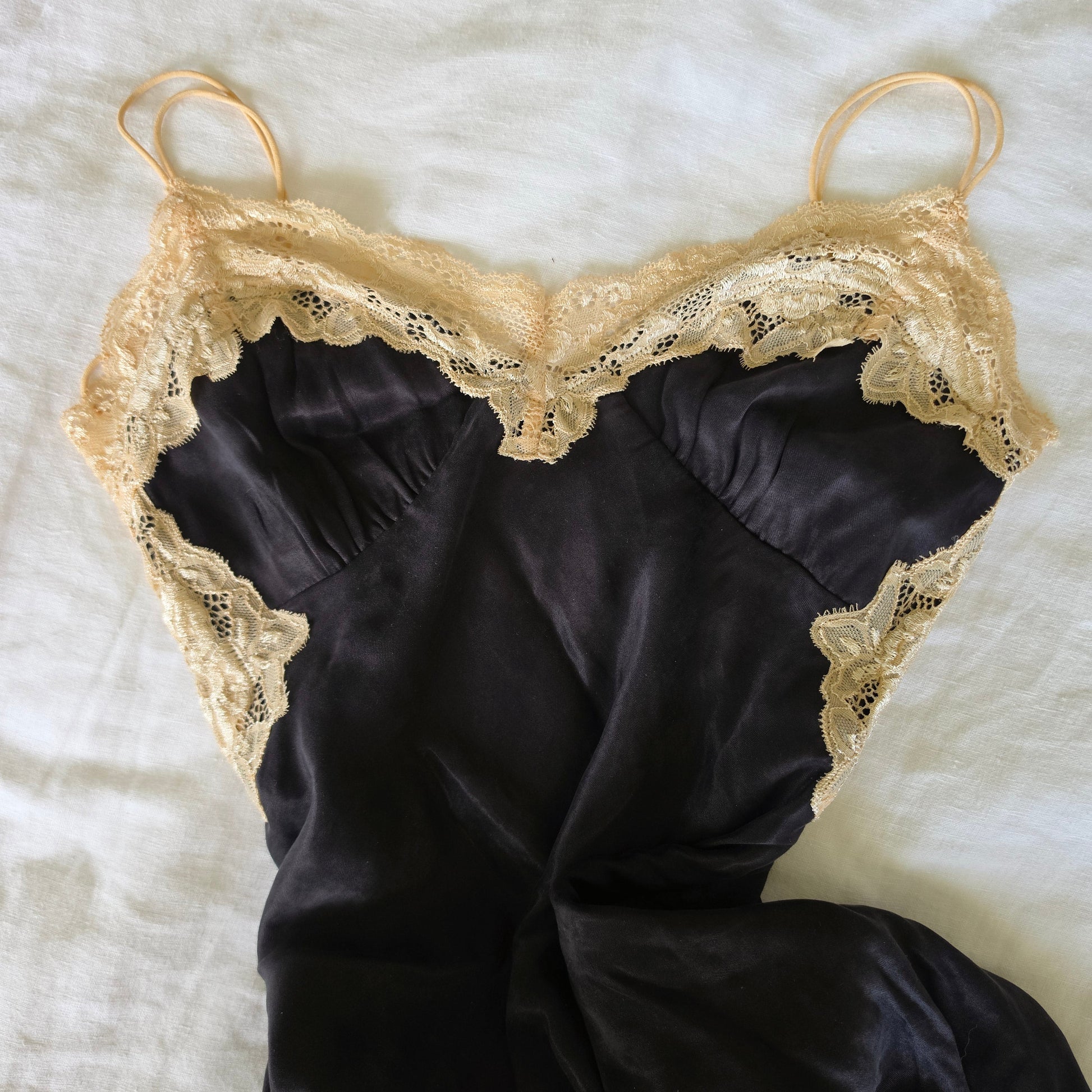 Flat lay image showing the lace panels and black slip dress with spaghetti straps.