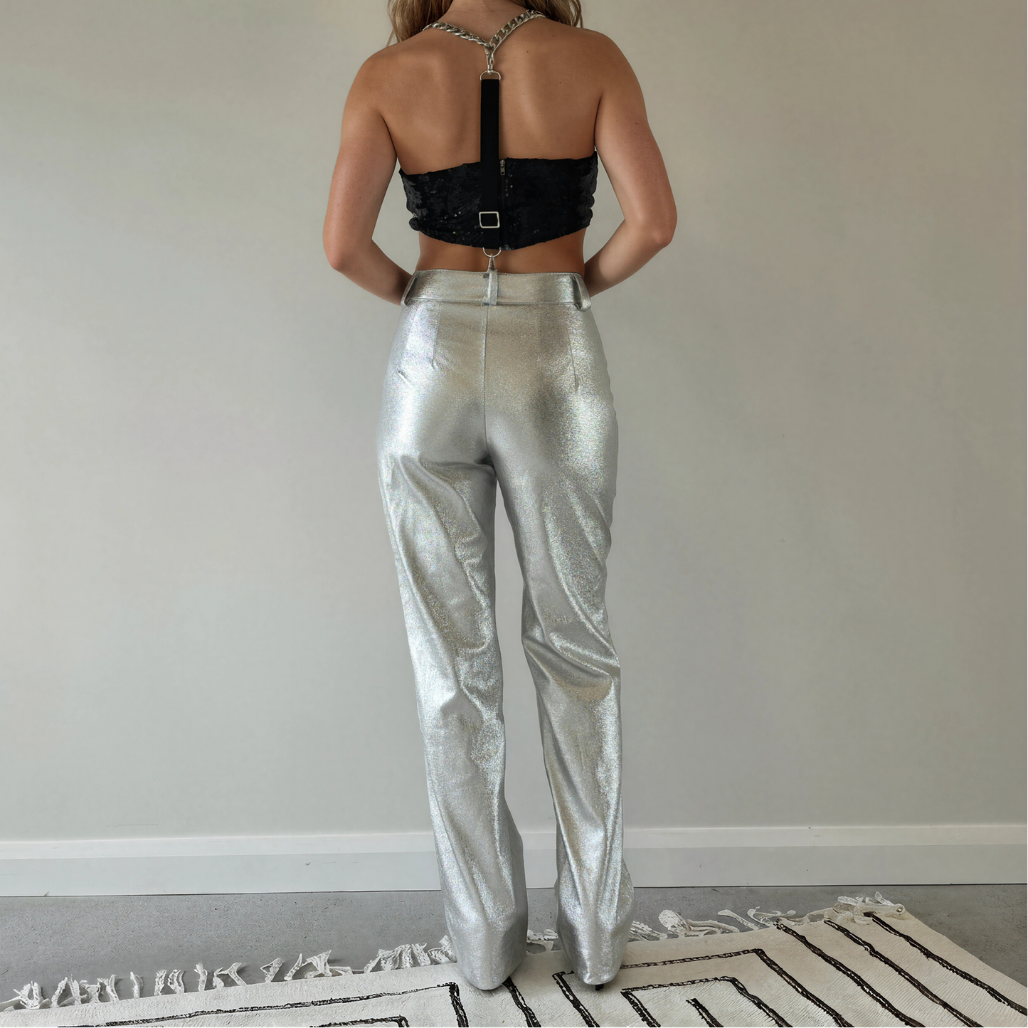 A woman stands with her back to the camera wearing shiny metallic silver Zara pants.