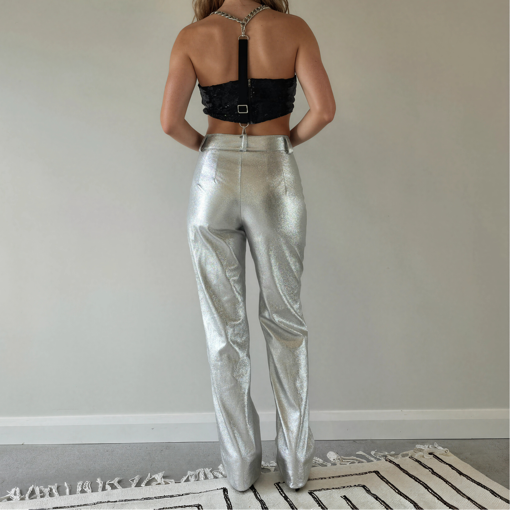 A woman stands with her back to the camera wearing shiny metallic silver Zara pants.