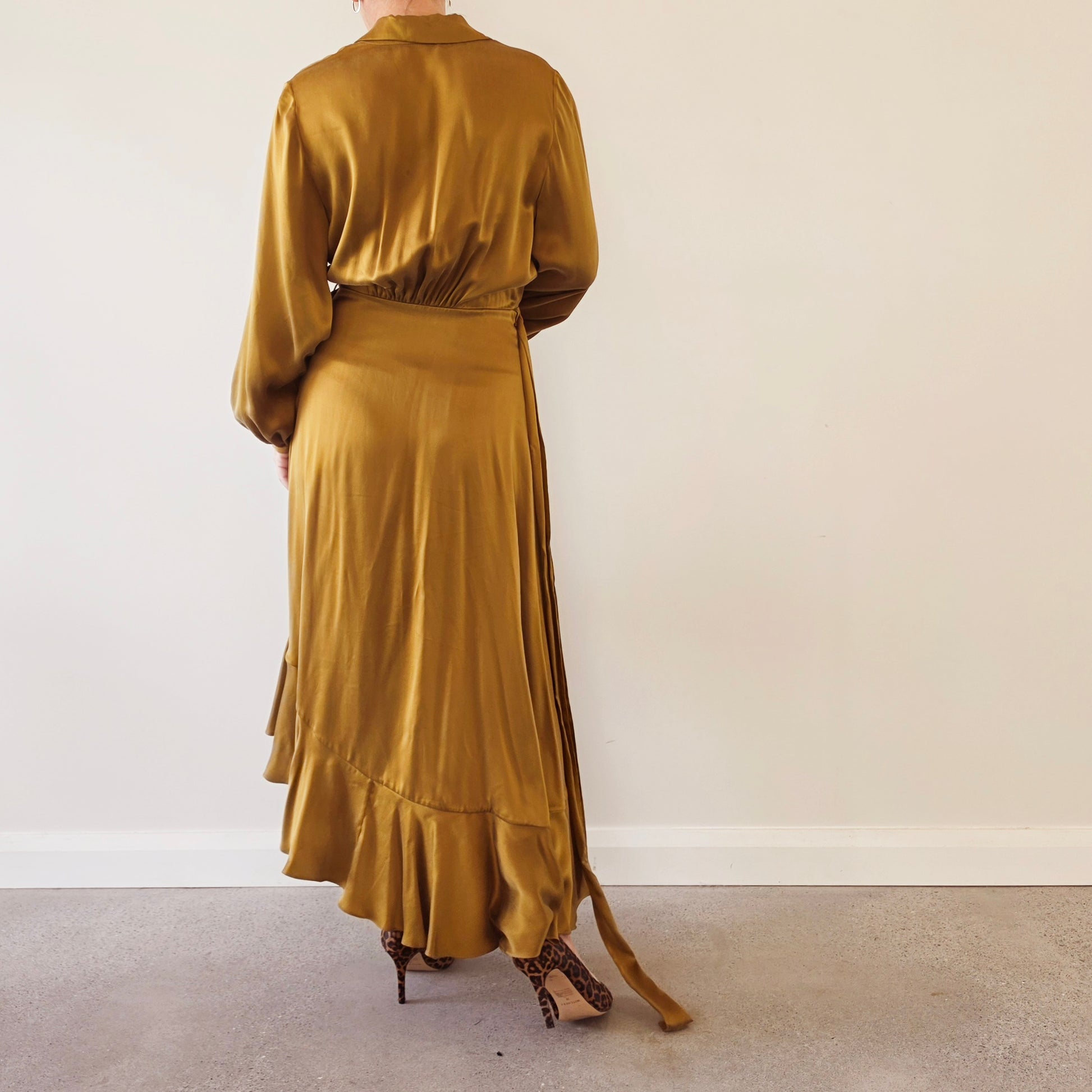 Image of model showing the back of the Zimmermann silk wrap midi dress with a ruffled hem, paired with leopard-print high heels.