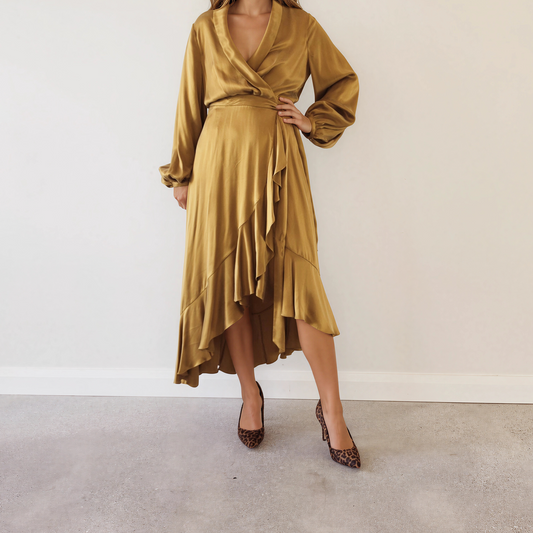 Image of a model in the Zimmermann long-sleeved, wrap-style silk midi dress in a shiny mustard-gold fabric